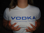 A person wearing a white short-sleeve t-shirt with 'VODKA Connecting People' printed in blue across the chest, photographed in a dark setting.