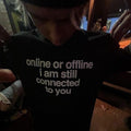 A person wearing a black t-shirt with the white printed text 'online or offline i am still connected to you', photographed in a dimly lit indoor setting.