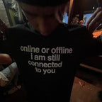A person wearing a black t-shirt with the white printed text 'online or offline i am still connected to you', photographed in a dimly lit indoor setting.