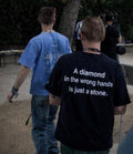 Person wearing a black t-shirt with a motivational quote in an outdoor setting. A Diamond In The Wrong Hands Is Just A Stone